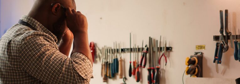 Carpenter inspecting wood in assembling shop, putting safety glasses on and picking tool from rack. Woodworking specialist in studio picking lumber block and carving gear for it, camera A